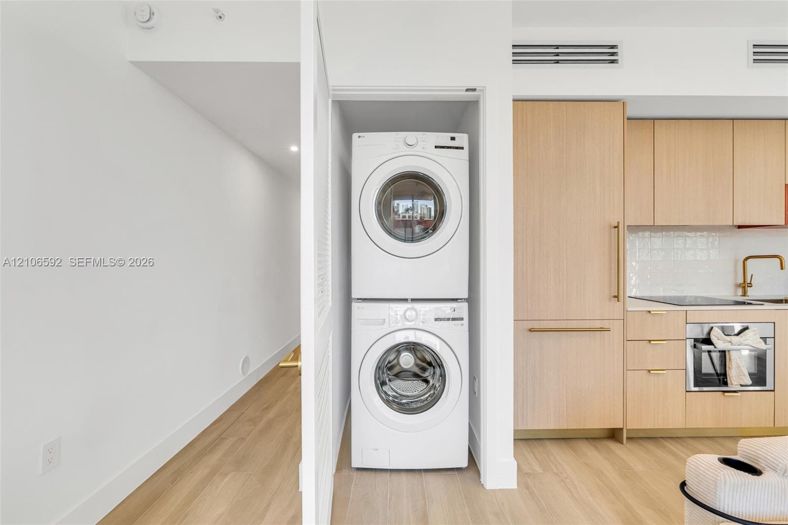 Stacked laundry center, flat-panel light wood cabinetry, integrated refrigerator, and light wood-finish flooring