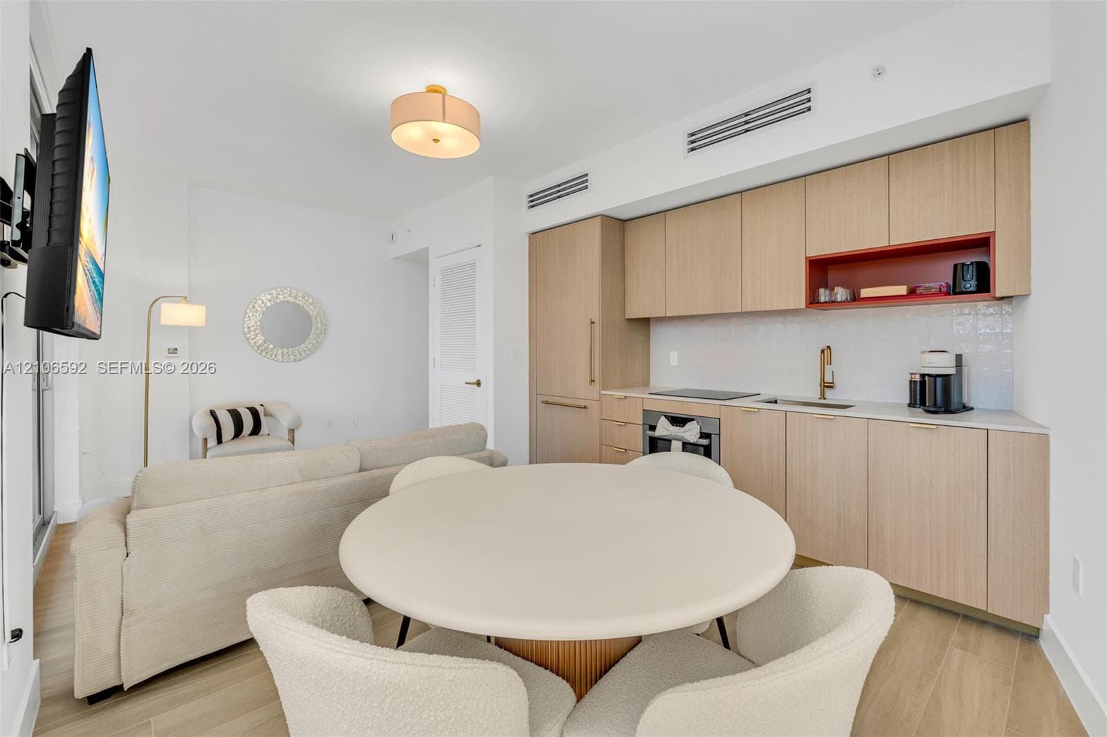 Kitchen featuring light wood-finish cabinetry, a contrasting red open shelf, an integrated cooktop, a built-in oven, and a gold-tone faucet, complemented by wood-finish flooring and a central drum-style pendant light