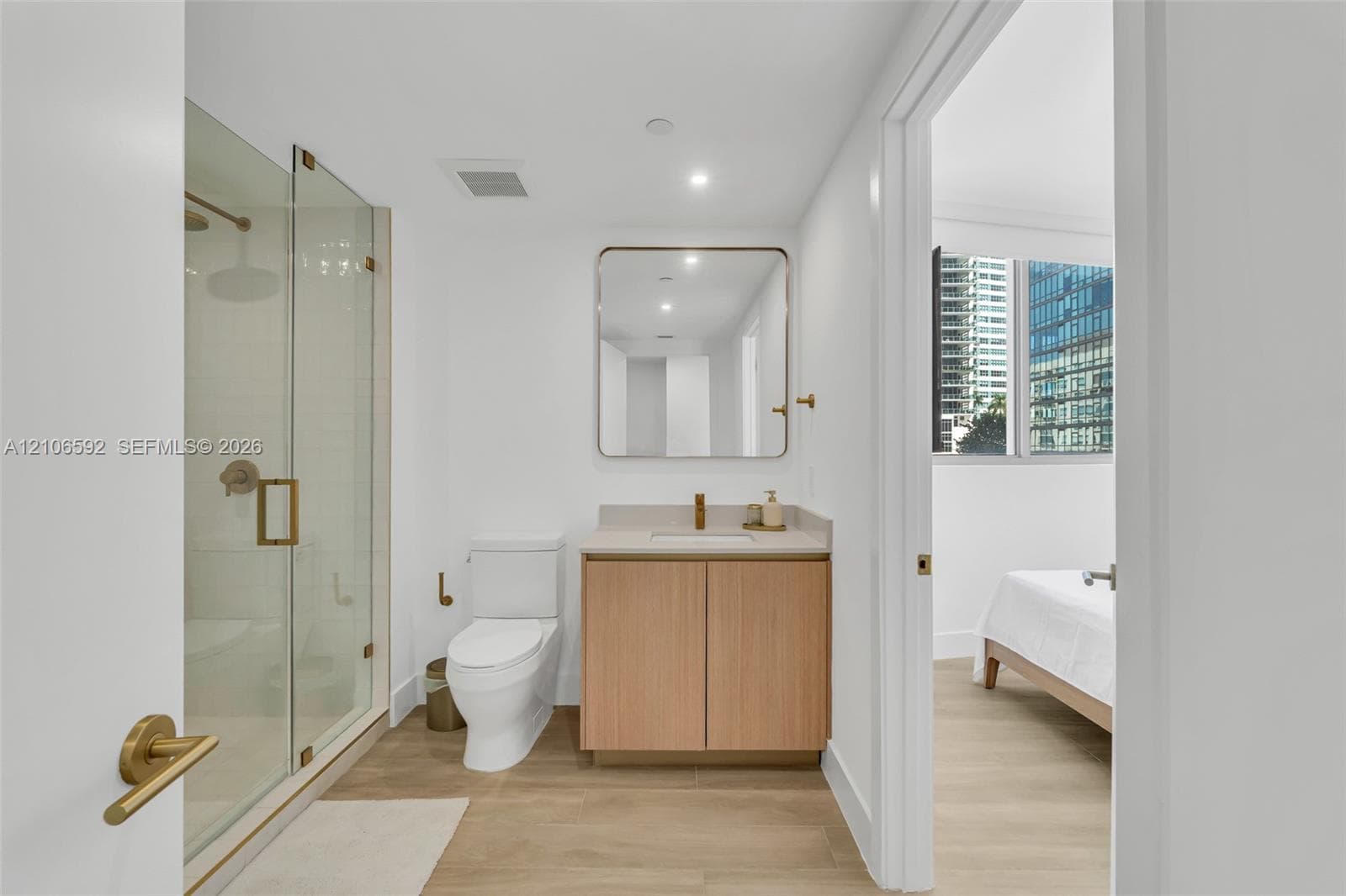 Bathroom featuring a glass-enclosed shower, light wood-finish cabinetry with a stone countertop, wall-mounted rectangular mirror with rounded corners, and metallic fixtures