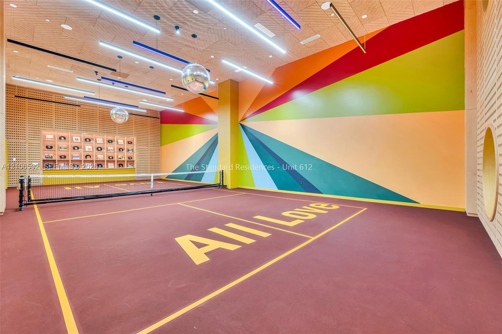 Indoor pickleball court featuring a specialized athletic surface, built-in display shelving, linear LED lighting, and decorative wall mural