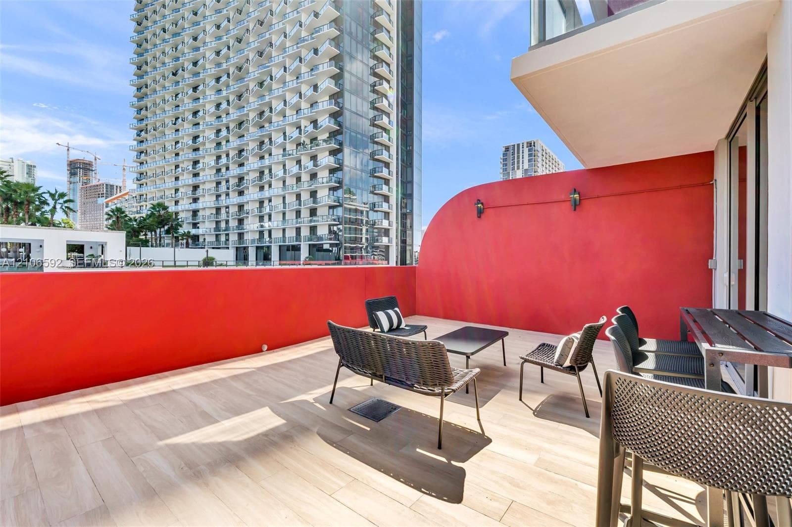 Expansive terrace featuring light wood-finish flooring, a curved red privacy wall, and wall-mounted exterior lighting