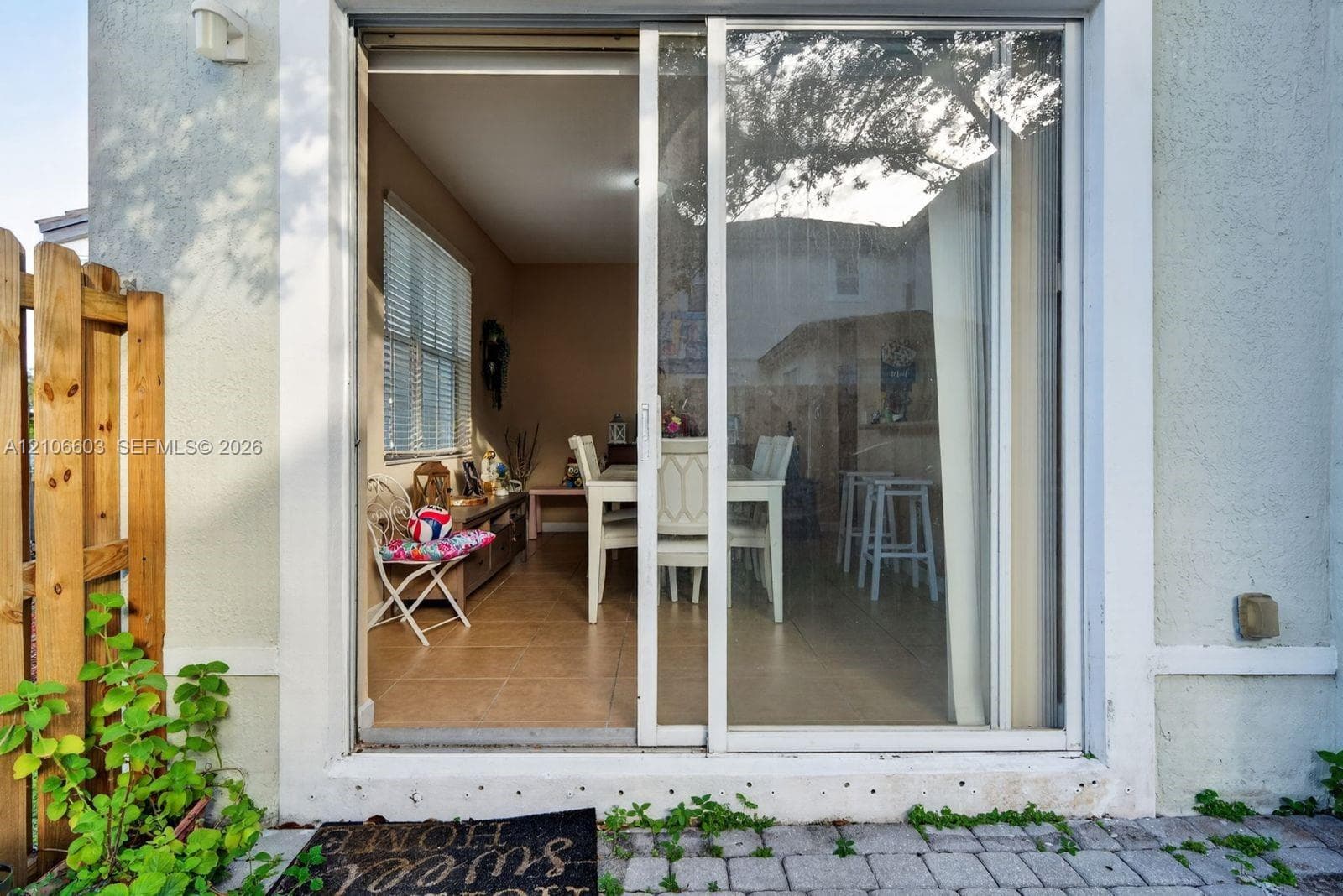 White-framed sliding glass door providing interior access, exterior stucco finish, and stone paver patio