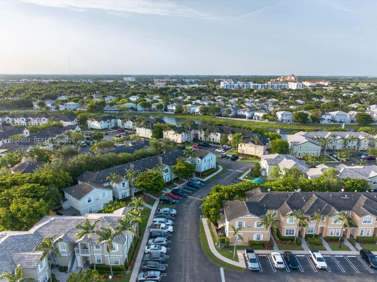Aerial perspective of a multi-building residential complex featuring tile-roofed exteriors, designated surface parking, mature palm landscaping, and integrated water features