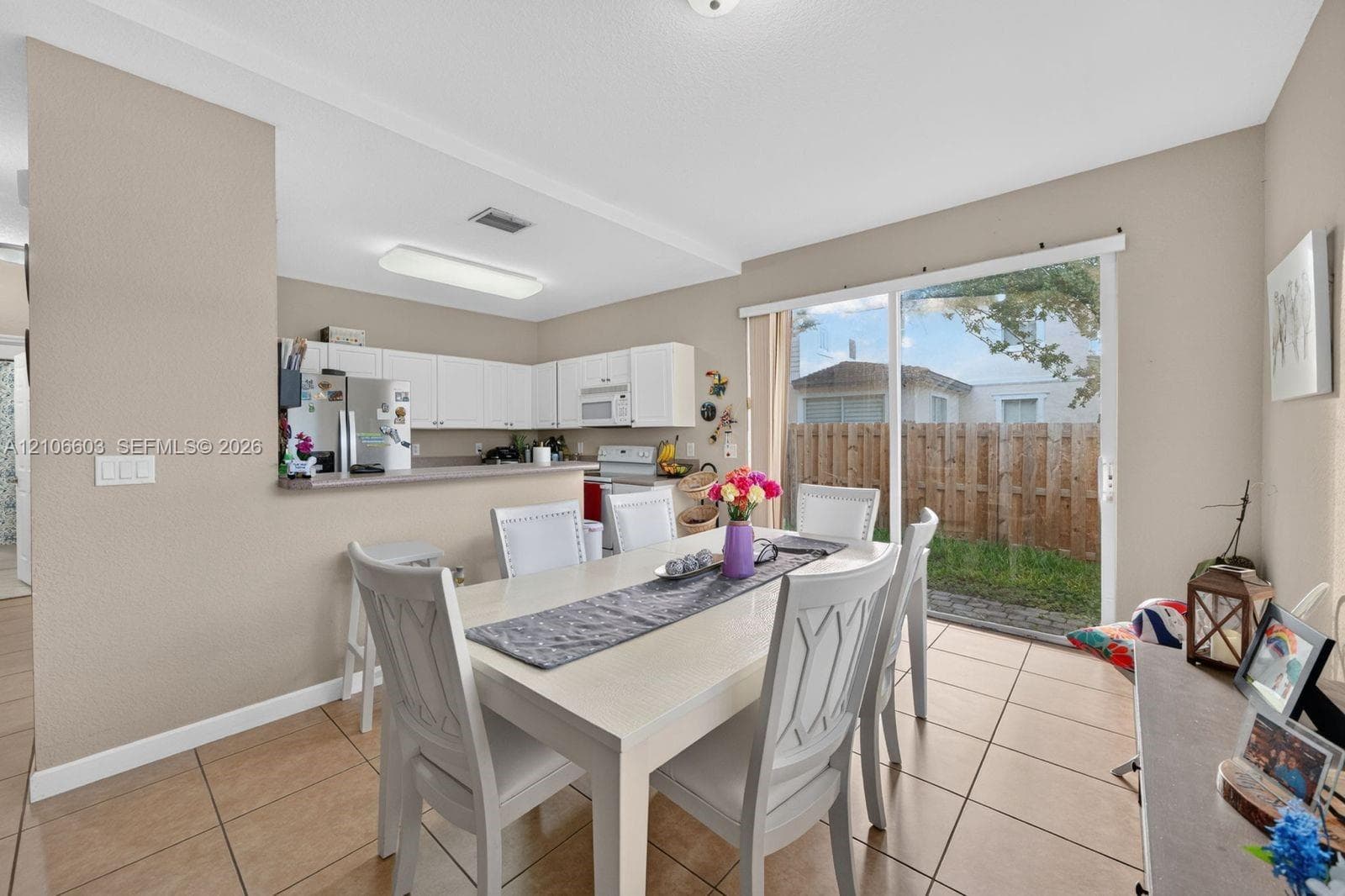 Dining area with neutral tile flooring, kitchen featuring white cabinetry and a breakfast bar, and glass sliding doors leading to a private outdoor space
