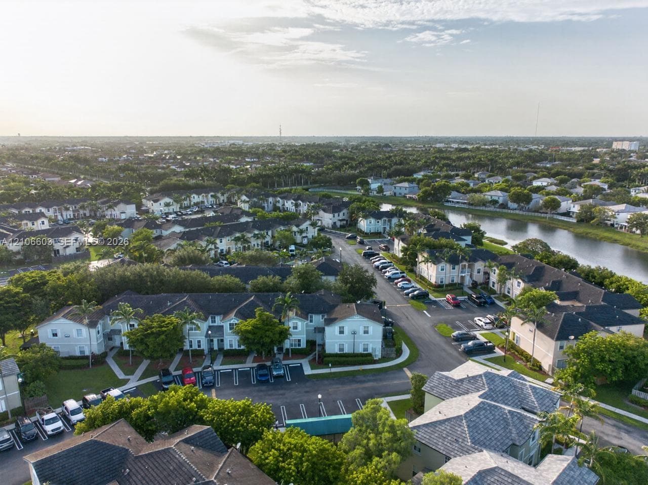 Aerial perspective of a multi-unit residential community featuring shingle-style roofing, paved parking areas, sidewalk pathways, and a water feature