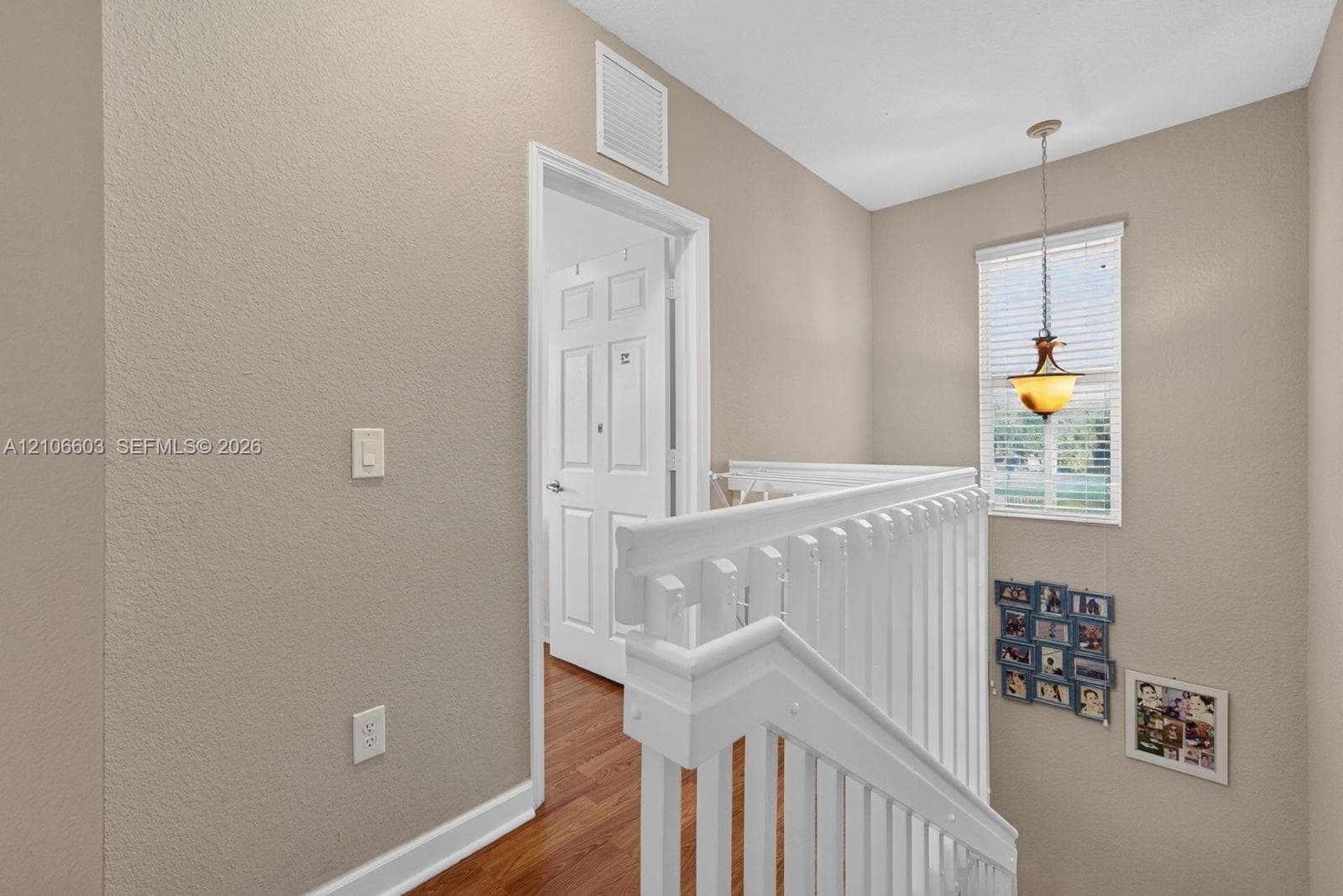 White wood railing, wood-finish flooring, neutral wall paint, and pendant lighting
