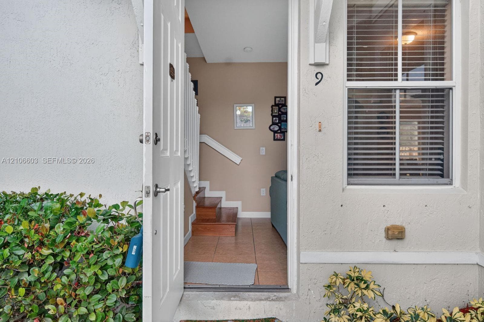 Entry featuring a hinged door with brushed metal hardware, ceramic tile flooring, and a staircase with wood-finished treads and a white painted railing
