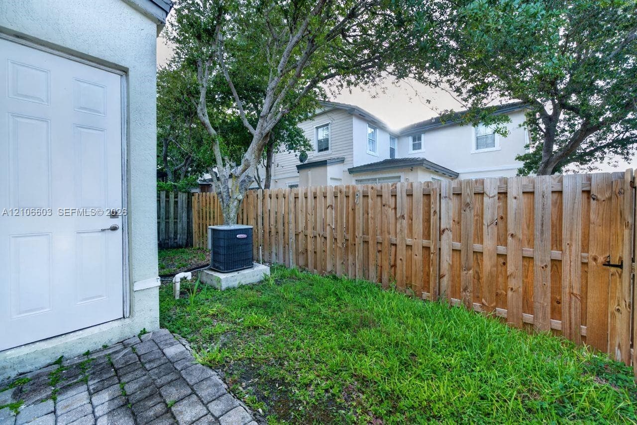 Side yard featuring a concrete paver walkway, wood fence, mature trees, and an external heating and cooling unit