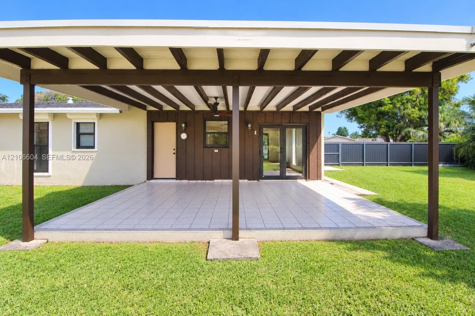 Covered patio featuring an exposed beam ceiling, tiled flooring, vertical wood-panel siding, and double glass-paneled exterior doors