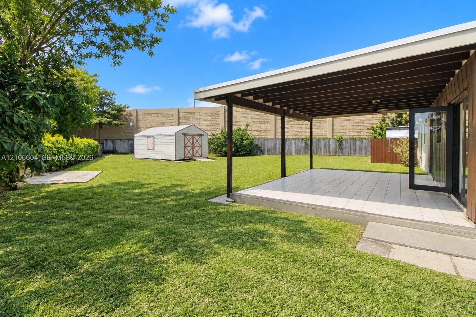 Backyard featuring a covered patio with tile flooring, an expansive lawn, a standalone storage shed, and masonry perimeter wall