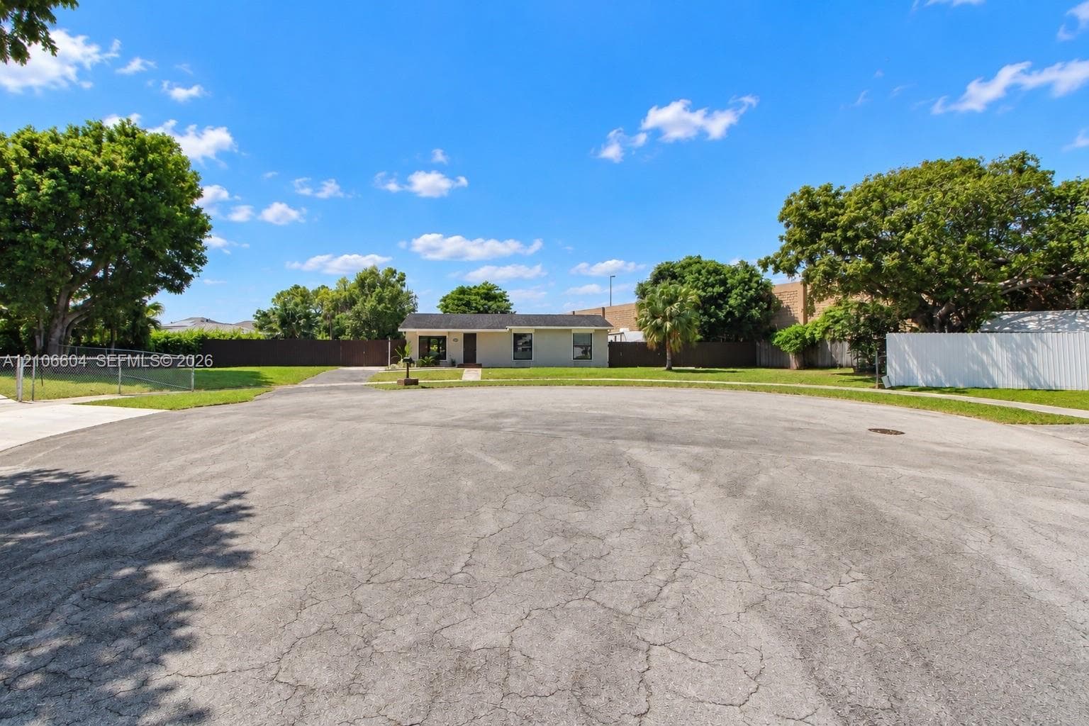 Single-story residence featuring a low-slope roof, expansive front lawn, mature trees, and perimeter fencing