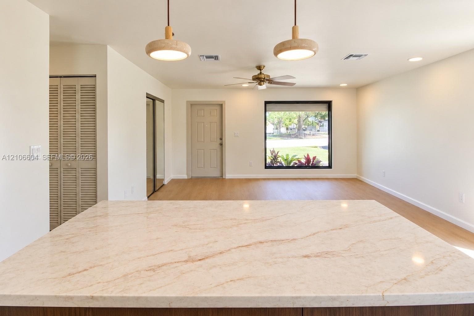 Solid-surface countertop with neutral veining, wood-finish flooring, dual pendant lighting, ceiling fan, and louvered closet doors