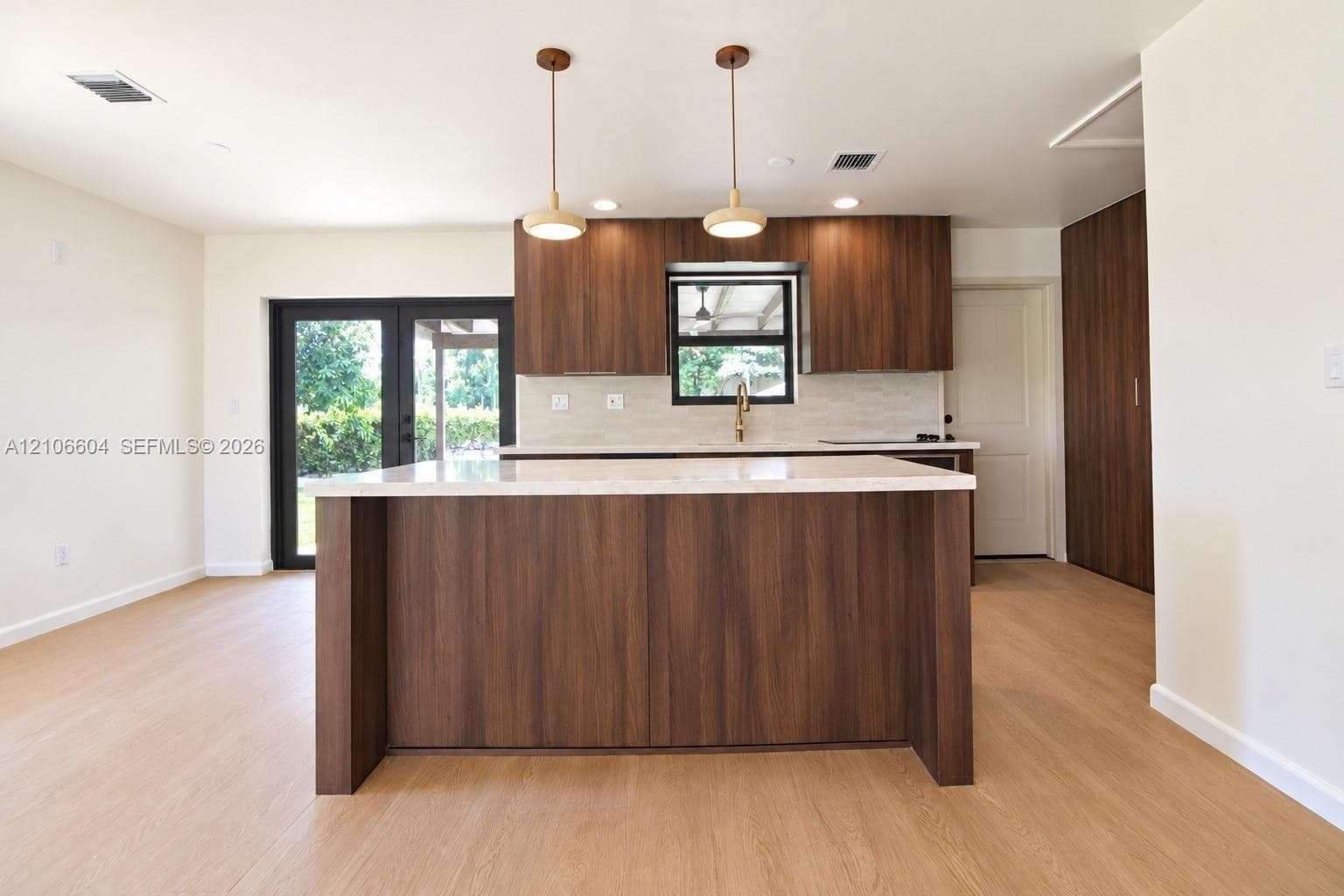 Kitchen featuring wood-finish cabinetry, a central island with a stone-surfaced countertop, dual pendant lights, and light-toned wood-finish flooring