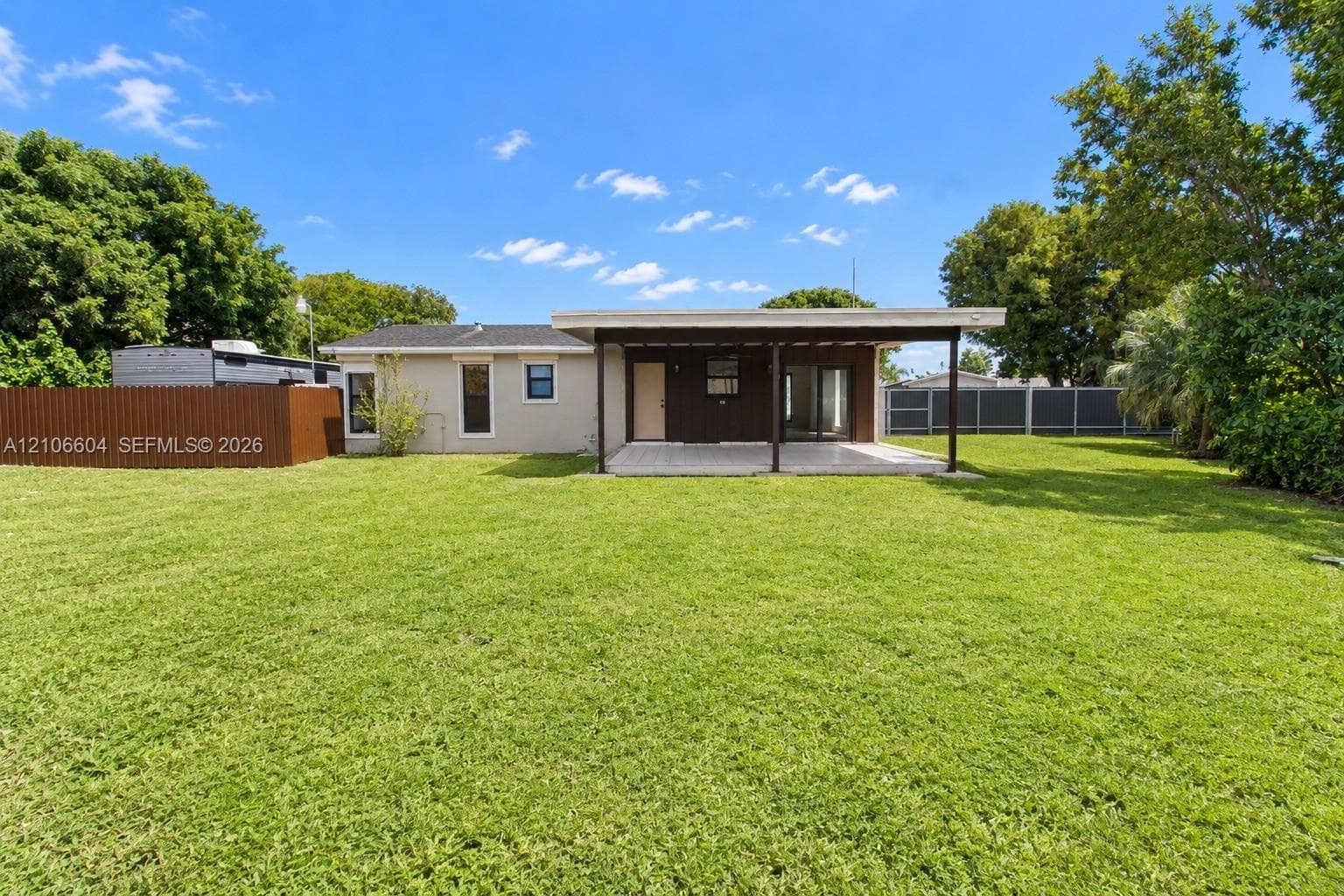Expansive backyard featuring a manicured lawn, covered patio, privacy fencing, and mature trees