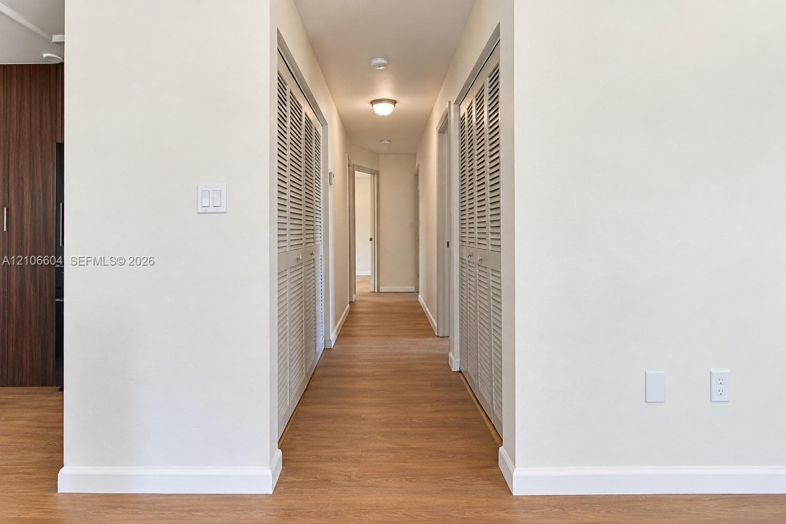 Hallway featuring wood-finish flooring, dual louvered-door closets, and flush-mount ceiling lighting