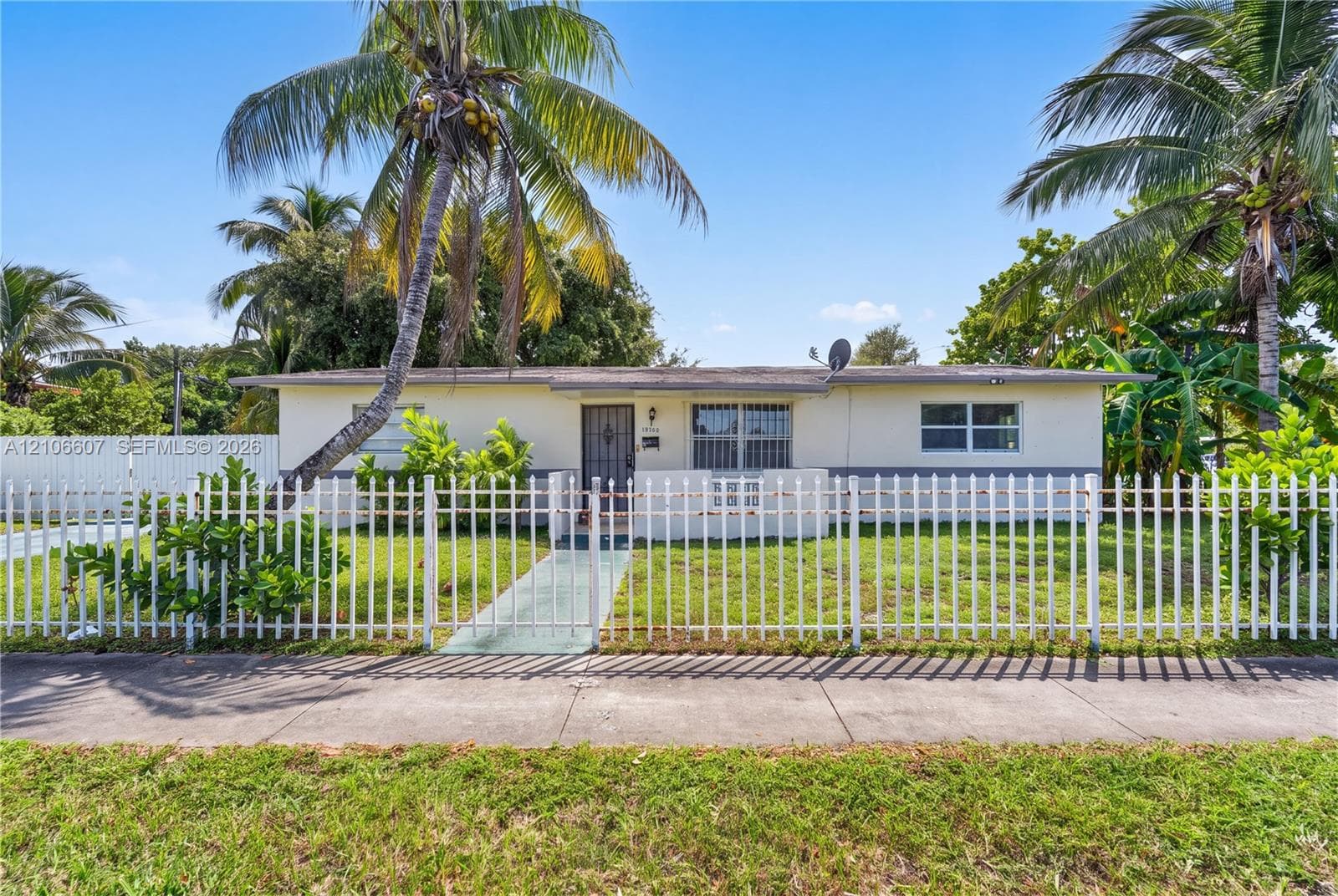 Single-story residence featuring a painted exterior, a concrete walkway, metal security bars on windows and door, and a white metal perimeter fence