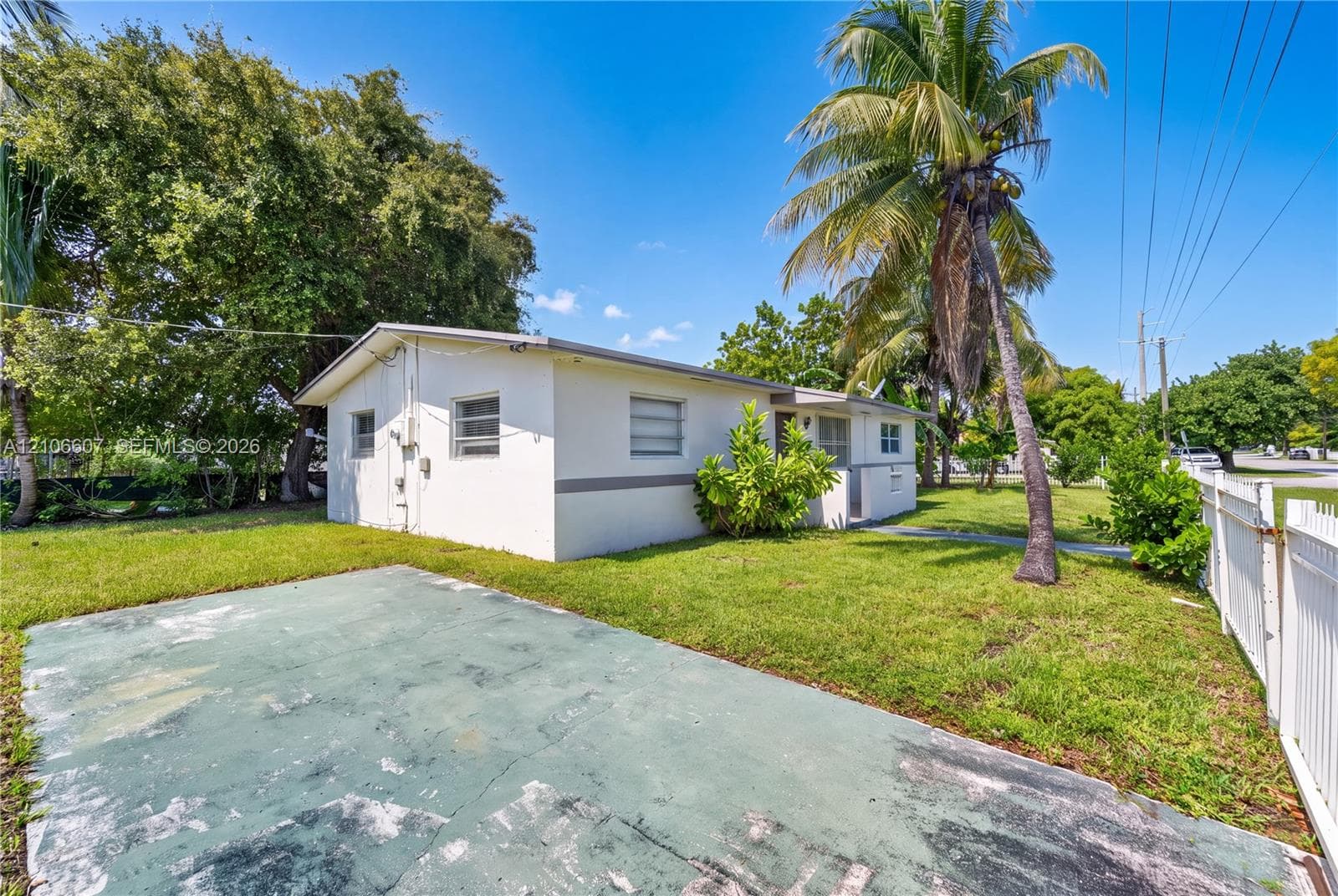 Stucco exterior residence featuring a concrete driveway, perimeter vinyl fencing, and mature palm trees set within a grass lawn