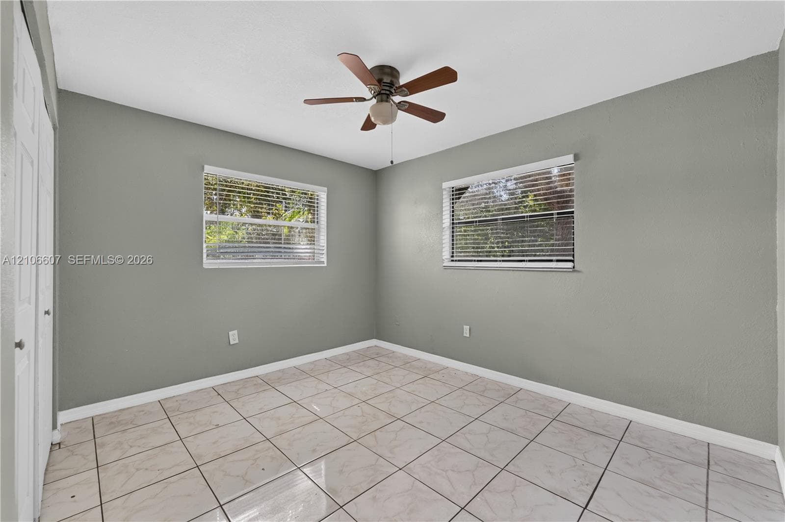 Neutral wall finish, tiled flooring, two windows with horizontal blinds, and a ceiling-mounted light fixture with fan blades
