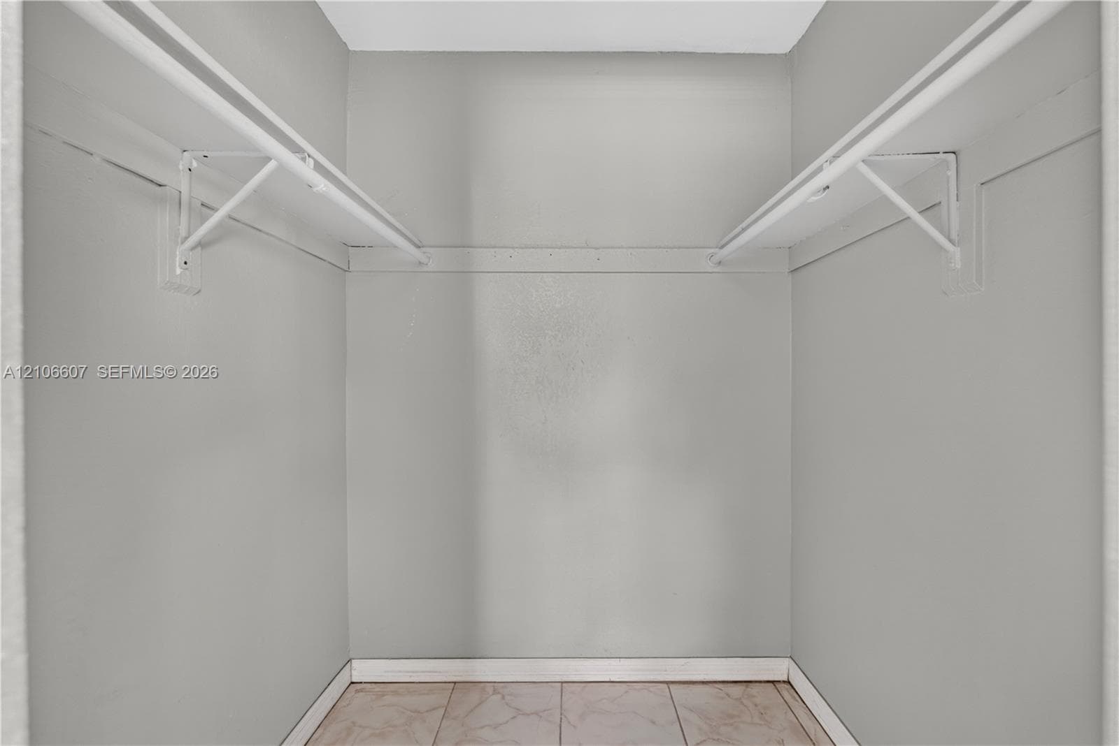 Walk-in closet featuring dual-level white shelving and tile flooring