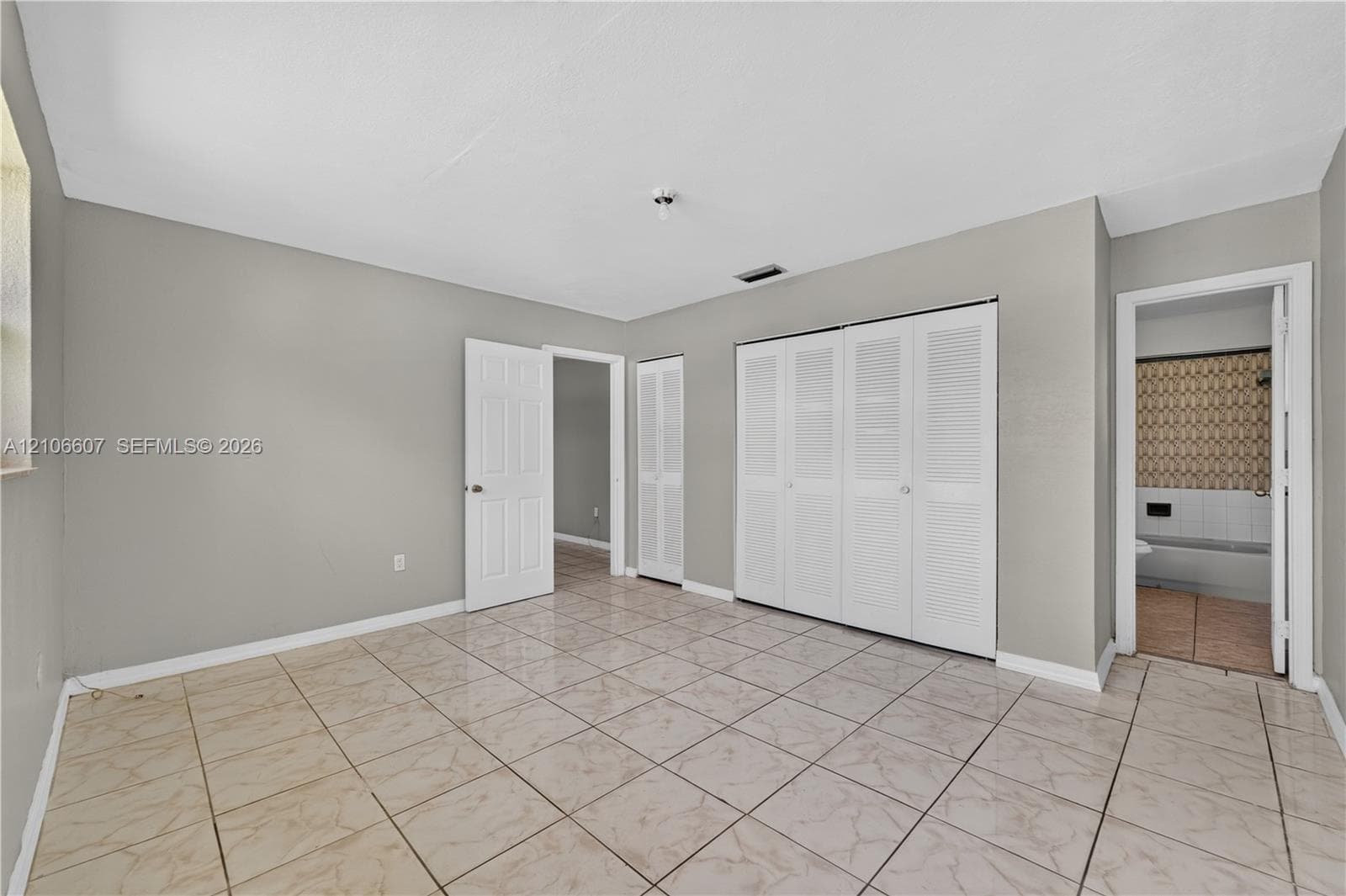 Neutral-toned interior featuring large-format ceramic tile flooring, multi-panel doors, and built-in closet storage with louvered doors