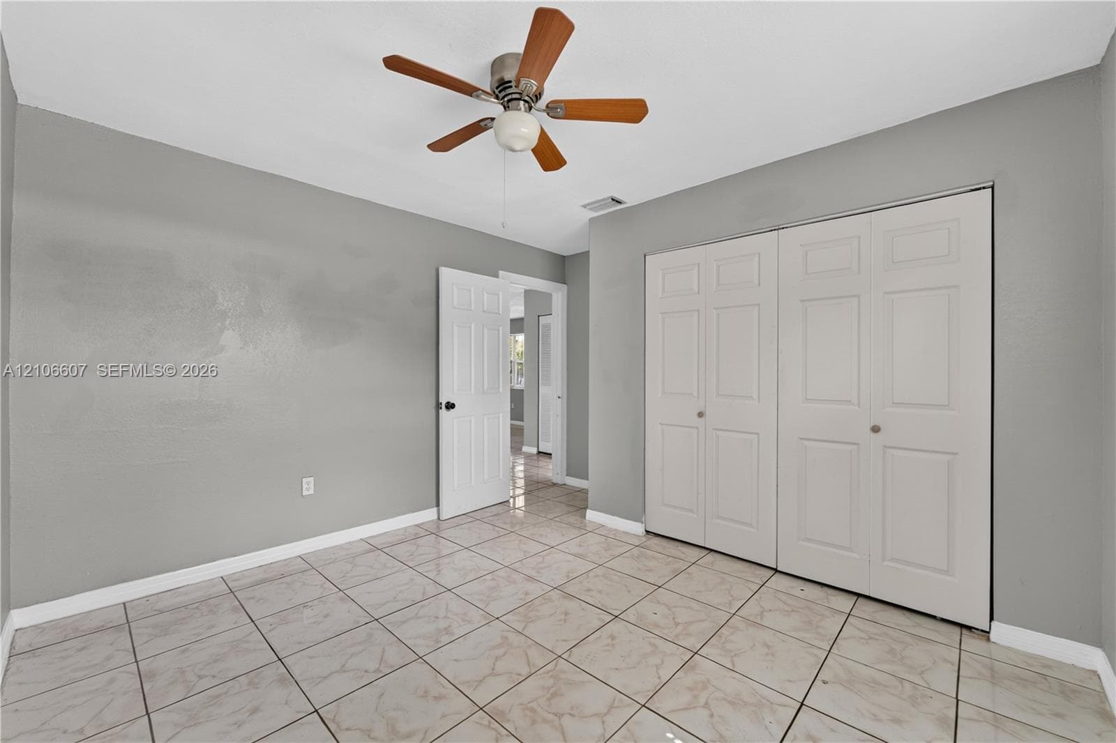 Neutral-toned interior room featuring tile flooring, a ceiling fan with light fixture, and double-panel closet doors
