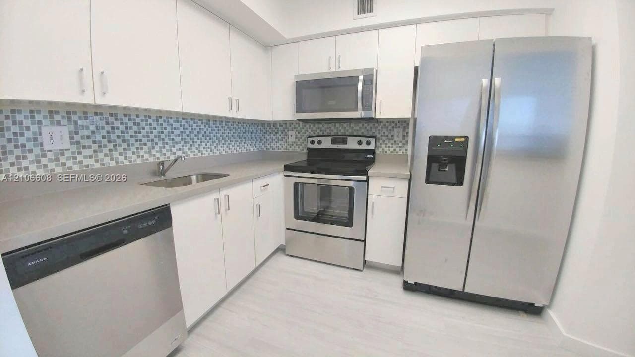 Kitchen featuring white cabinetry, solid-surface countertops, stainless steel appliances, and a mosaic tile backsplash