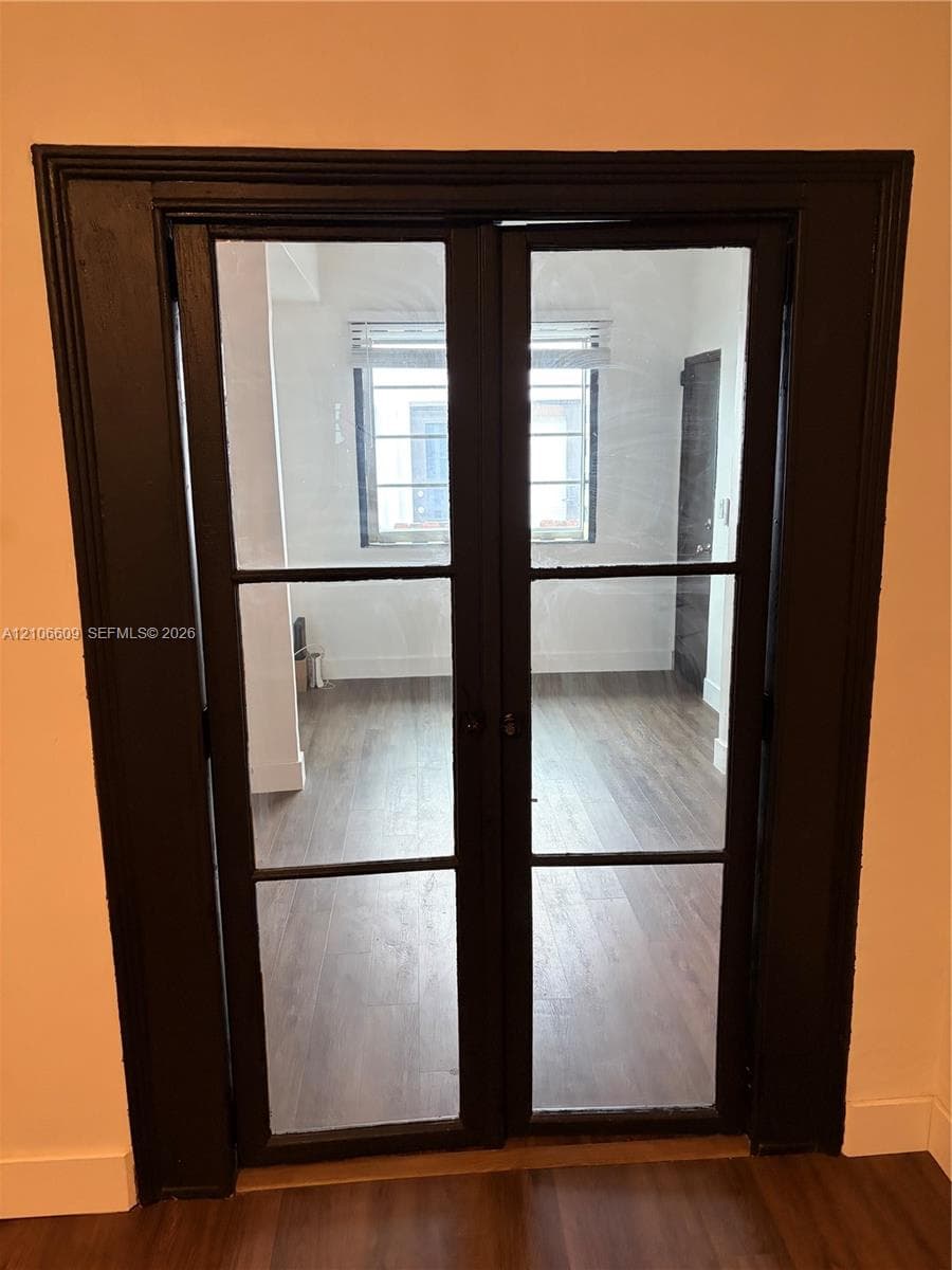 Double French doors featuring black-finished frames, glass panes, and wood-finish flooring