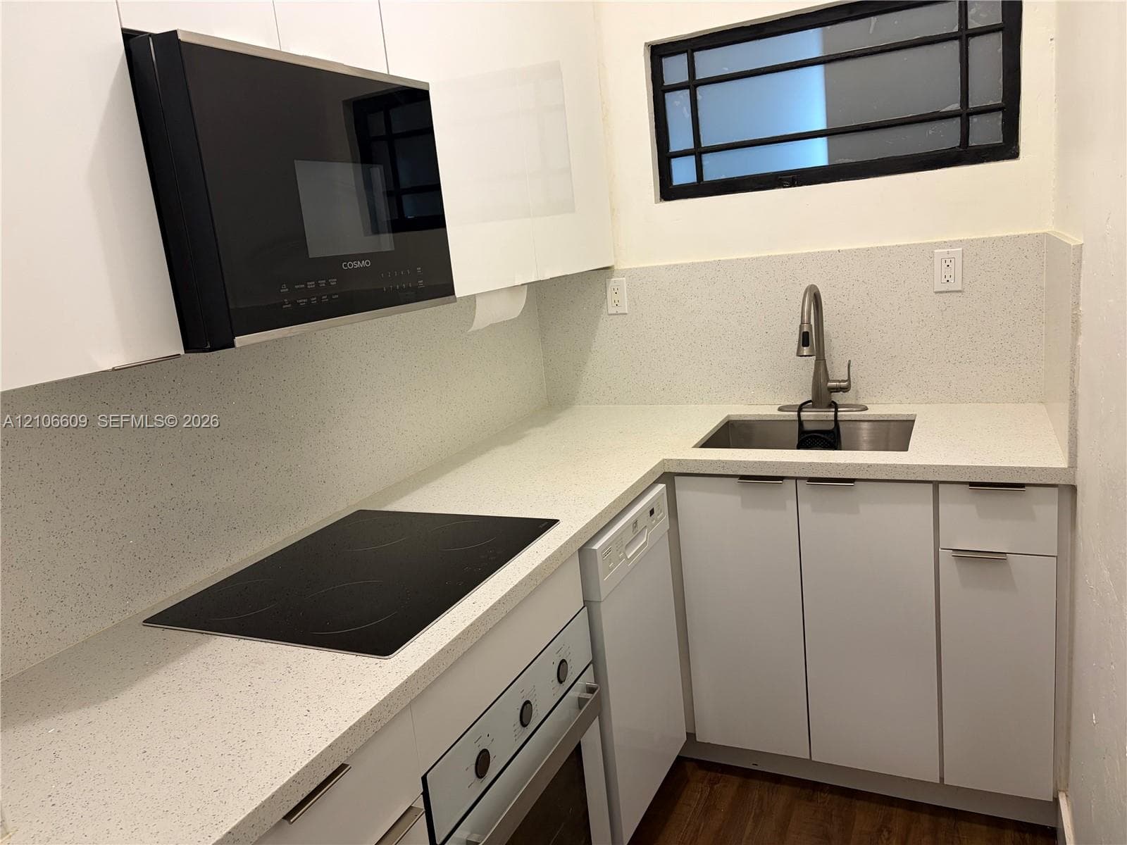 Kitchen featuring flat-panel white cabinetry, light-toned composite countertops, a stainless steel undermount sink with a gooseneck faucet, integrated cooktop, and a built-in microwave