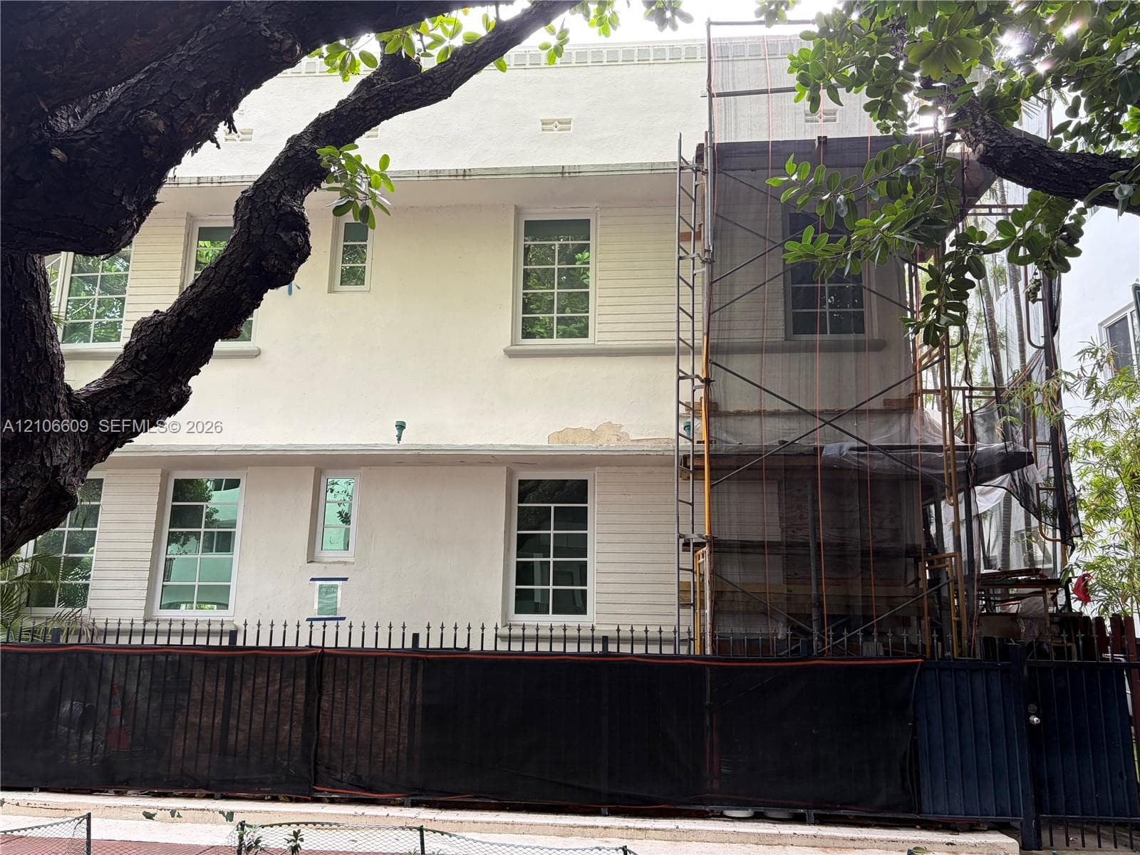 Two-story exterior featuring a light-colored stucco facade, multi-lite grid windows, and a metal perimeter fence