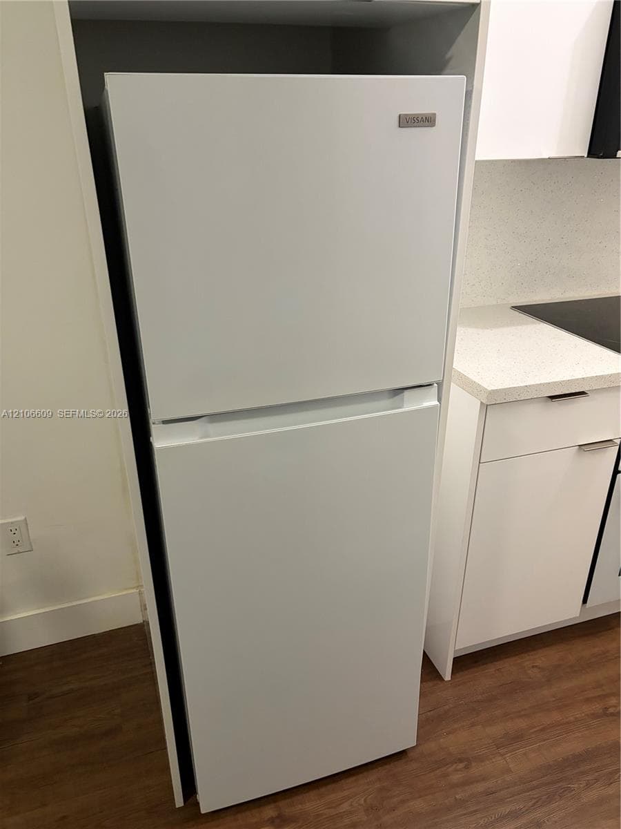 Top-mount refrigerator, white cabinetry, solid-surface countertop, and wood-finish flooring