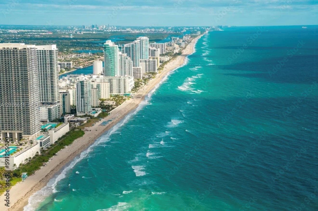 Aerial perspective of a high-rise residential corridor situated along a coastal shoreline, featuring direct ocean access and expansive water frontage