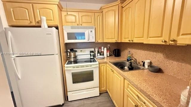 Kitchen featuring light-tone wood cabinetry, solid-surface countertops, a stainless steel undermount sink, and white appliances including a range and microwave
