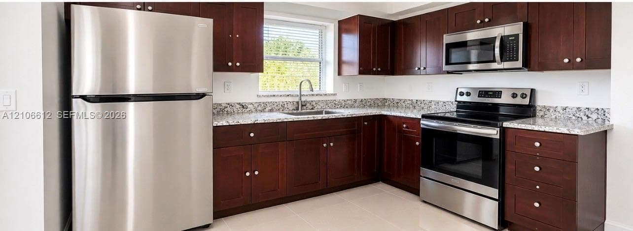 Kitchen featuring dark wood cabinetry, light stone-patterned countertops, stainless steel appliances, and tile flooring