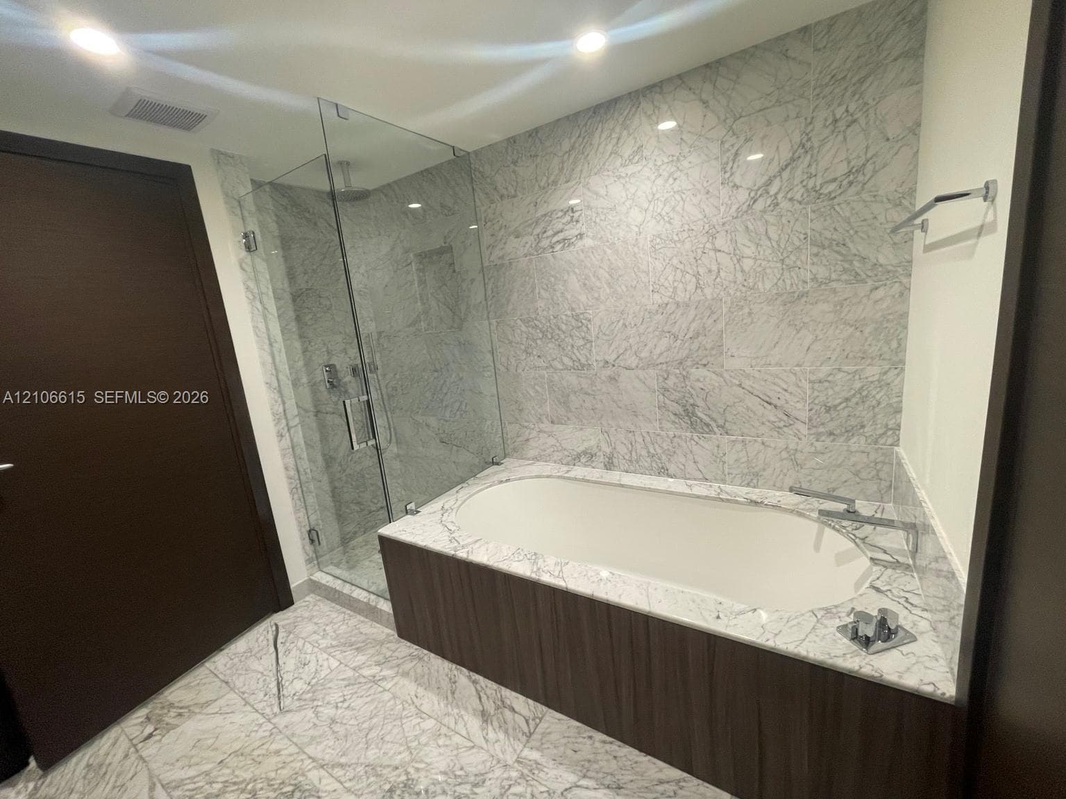 Soaking tub with stone-patterned surround, walk-in glass-enclosed shower, stone-finish flooring, and recessed ceiling lighting