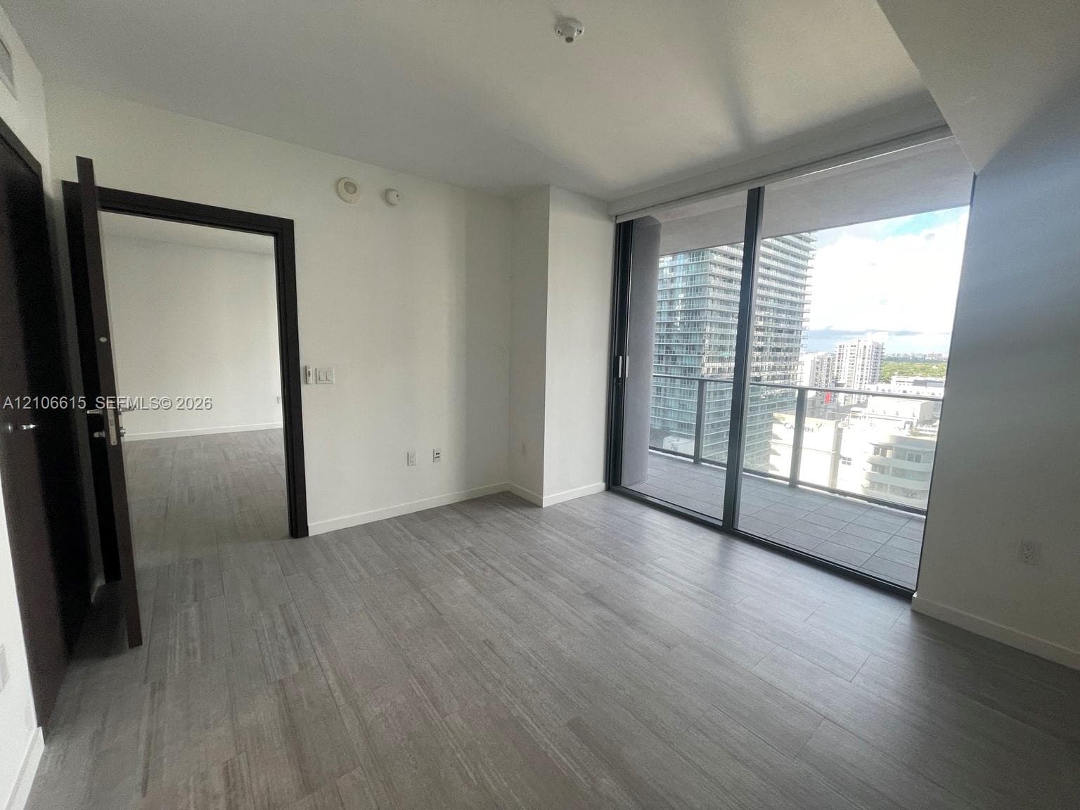 Wood-finish flooring, floor-to-ceiling glass sliding doors, and a private balcony featuring a metal railing
