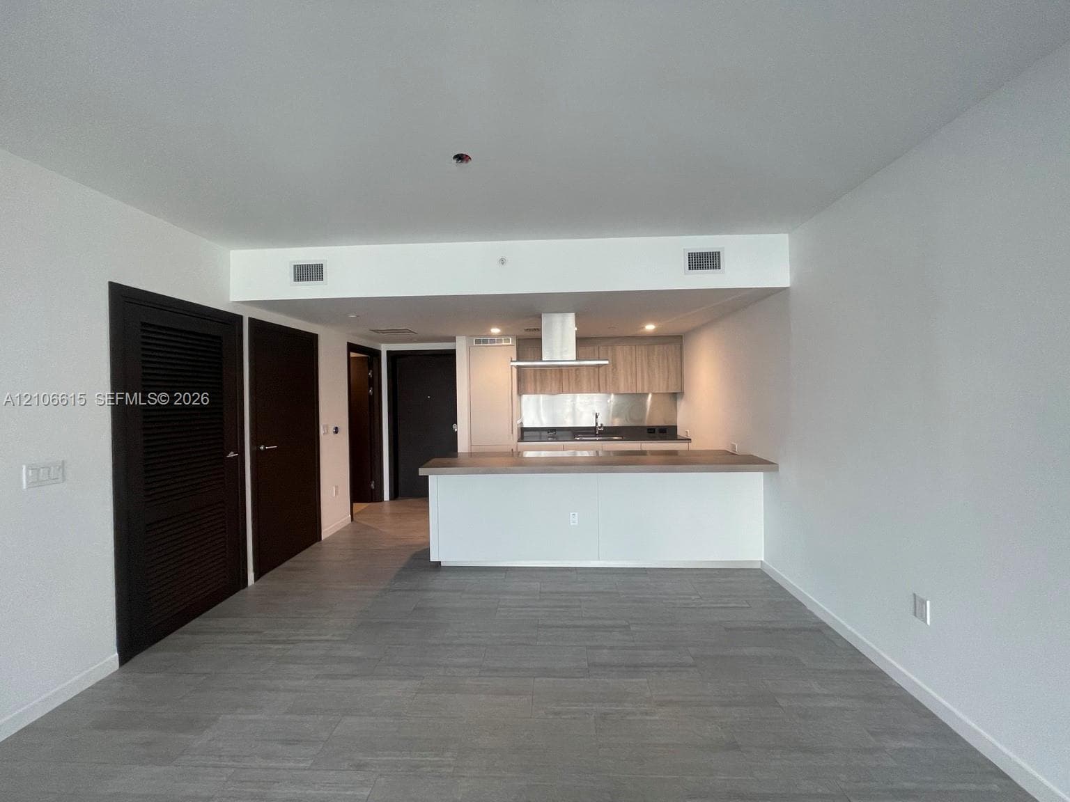 Open kitchen featuring a central island, solid-surface countertops, wood-finish cabinetry, a stainless steel range hood, and tile flooring