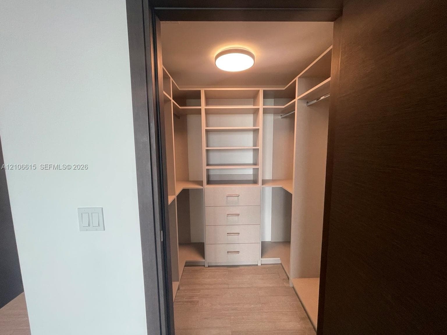 Walk-in closet featuring custom light-finish built-in cabinetry, floor-to-ceiling shelving, integrated storage drawers, and ceiling-mounted flush light fixture