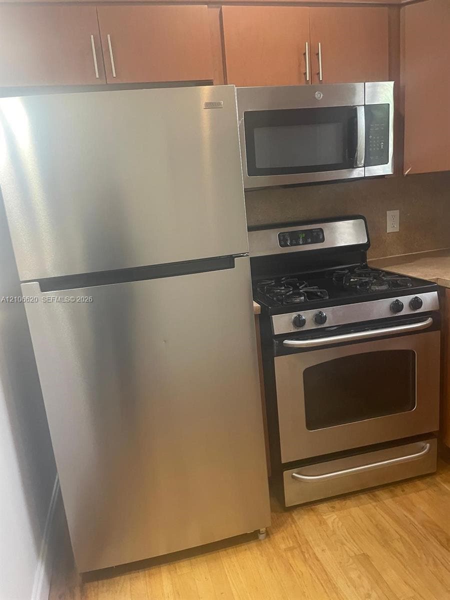 Stainless steel refrigerator, gas range, and over-the-range microwave, complemented by wood cabinetry and wood-finish flooring