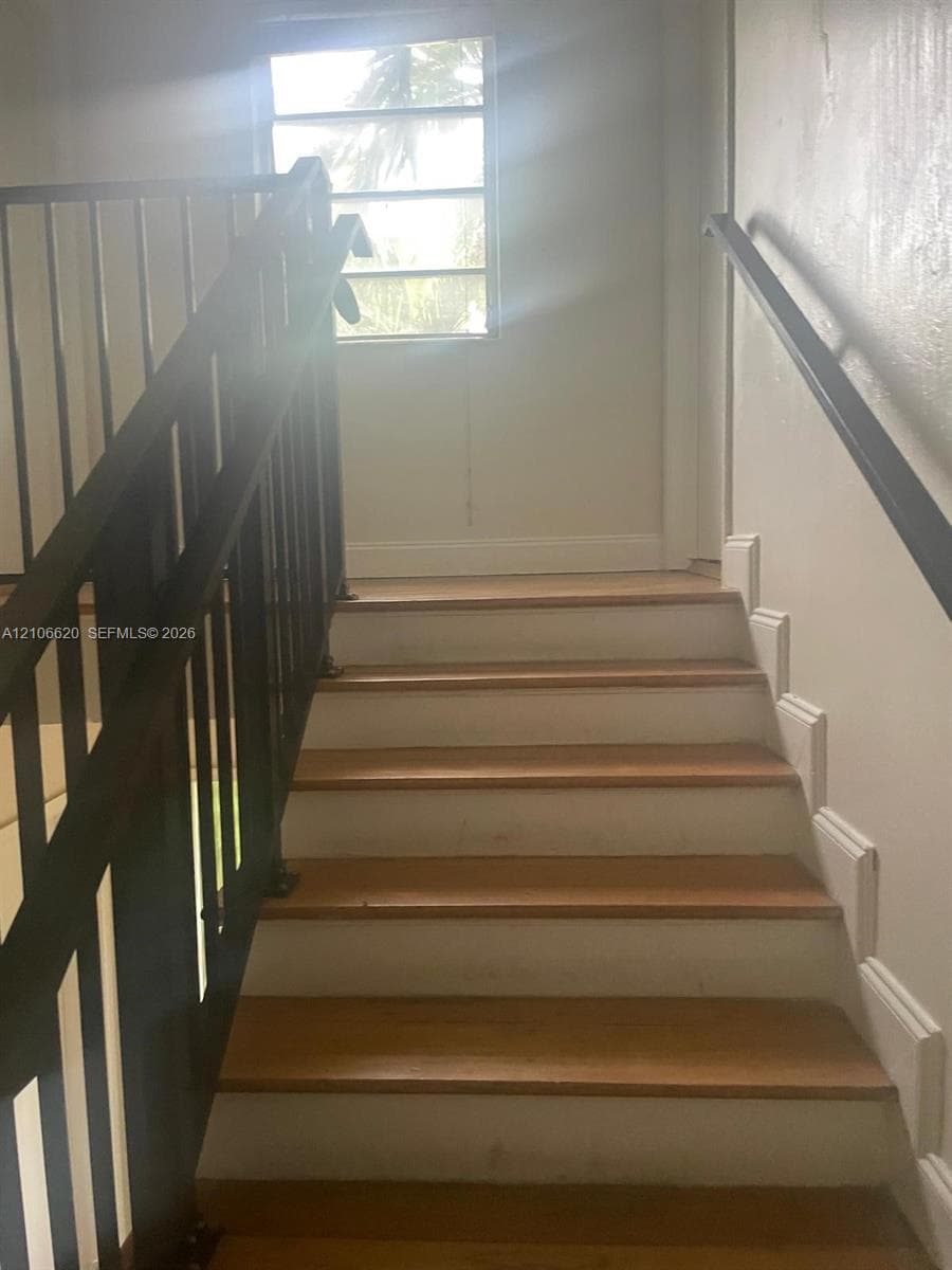 Staircase featuring wood-finish treads, white risers, and black metal handrails