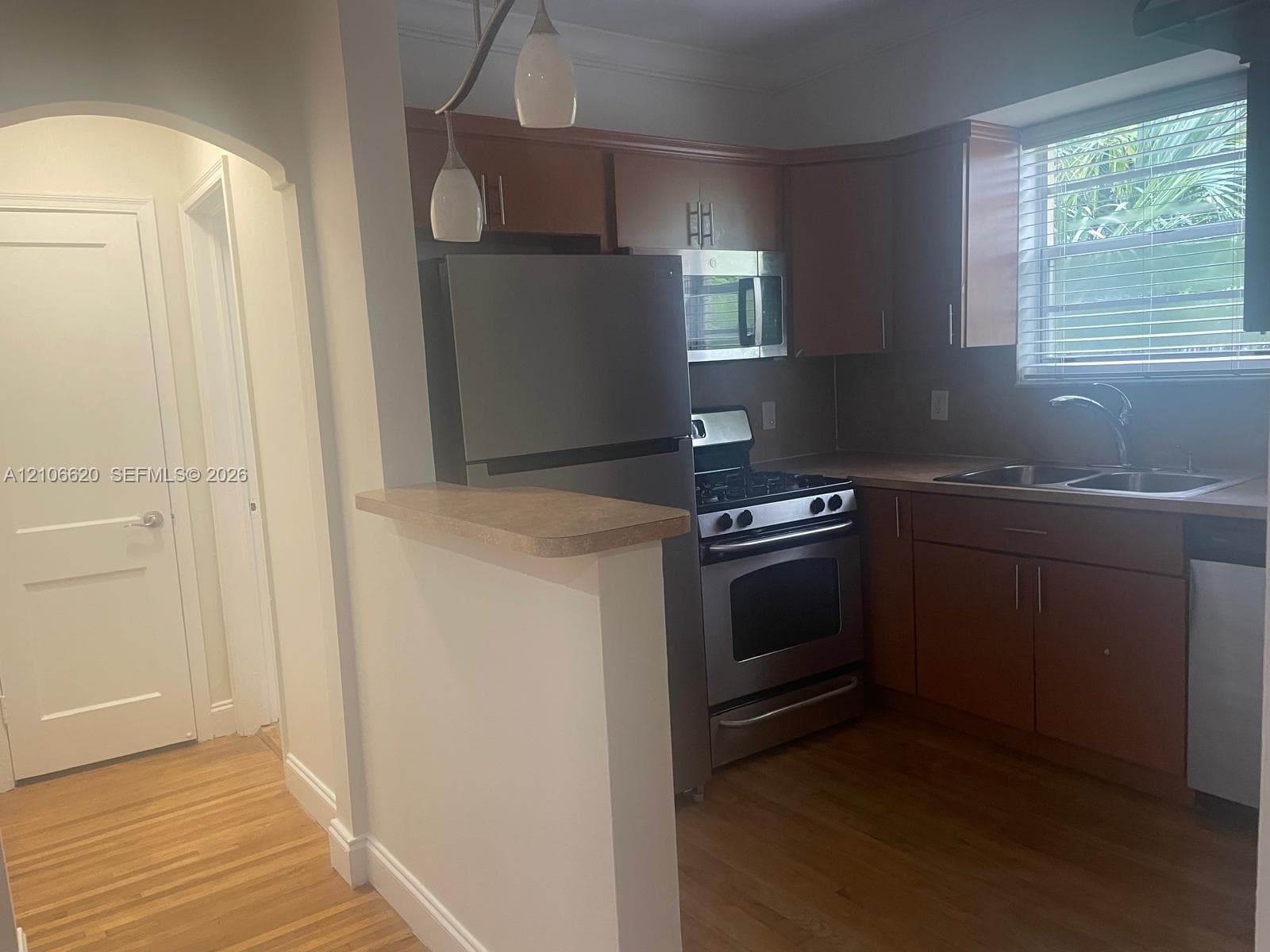 Kitchen featuring wood cabinetry, stainless steel appliances, wood-finish flooring, a pass-through counter, and arched entryway