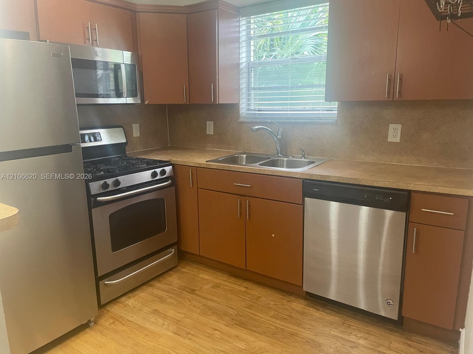 Kitchen featuring wood-finish cabinetry, stainless steel appliances, double-basin sink with pull-down faucet, solid-surface countertops, and wood-finish flooring