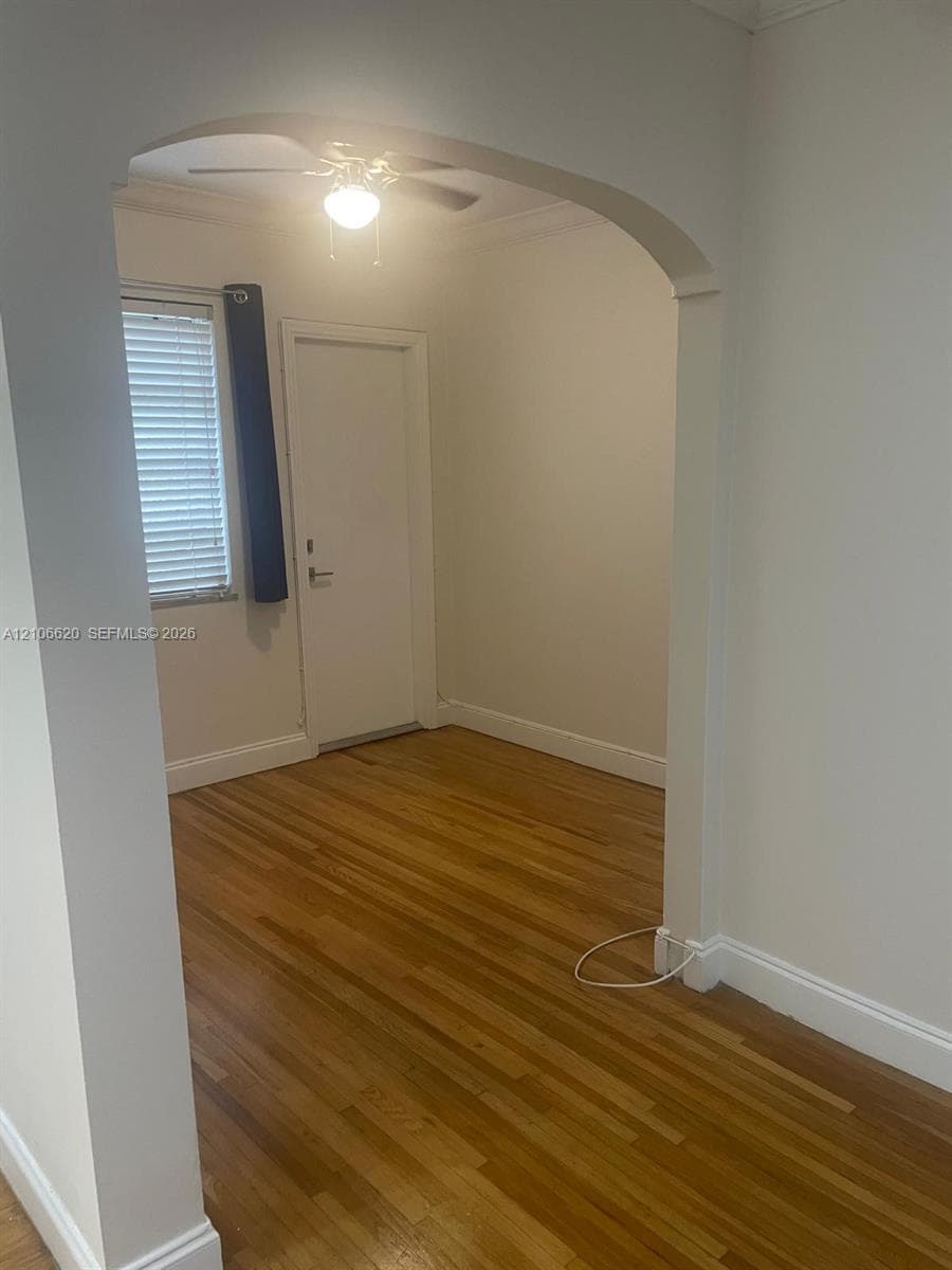 Interior space featuring an arched entryway, wood-finish flooring, a ceiling-mounted light fixture, and horizontal window blinds