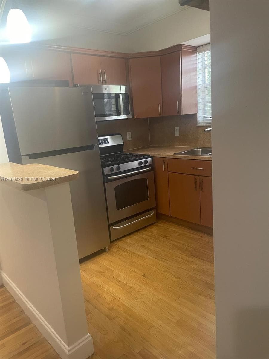 Kitchen featuring wood-finish cabinetry, stainless steel appliances, a gas range, and wood-finish flooring