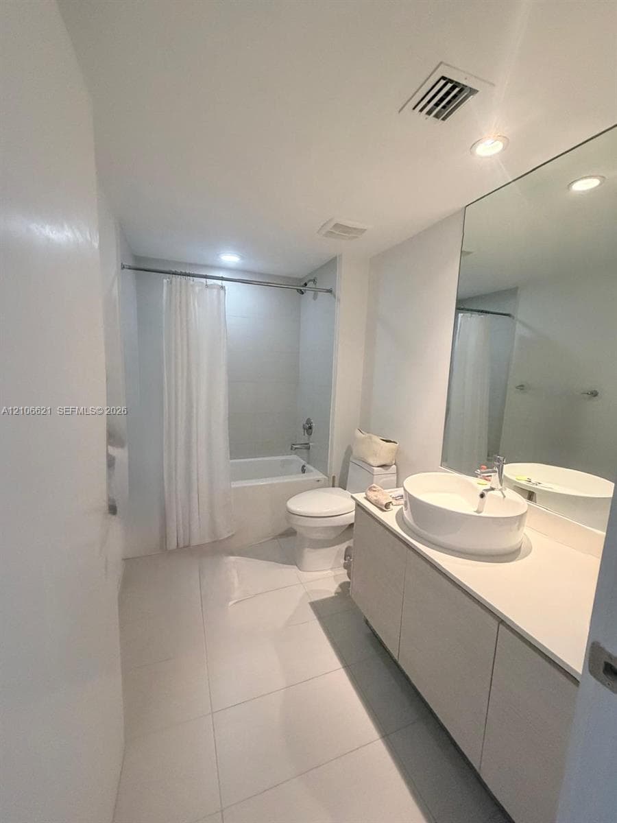 Bathroom featuring a vanity with a white composite countertop, an oval vessel sink, large-format tile flooring, a soaking tub with an integrated shower, and a full-height wall mirror