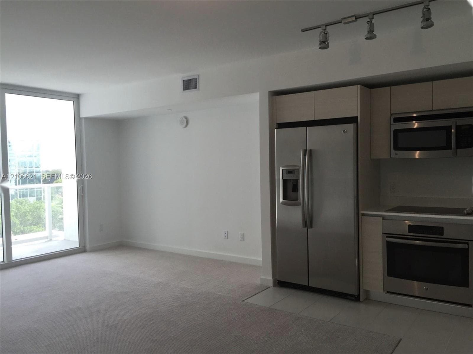 Kitchen featuring flat-panel cabinetry, stainless steel appliances, and integrated track lighting, complemented by a floor-to-ceiling glass door