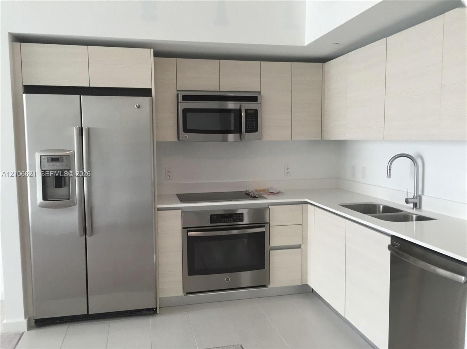 Kitchen featuring light wood-finish cabinetry, white solid-surface countertops, and a suite of stainless steel appliances, including an integrated refrigerator, built-in microwave, range, and dishwasher with a gooseneck faucet