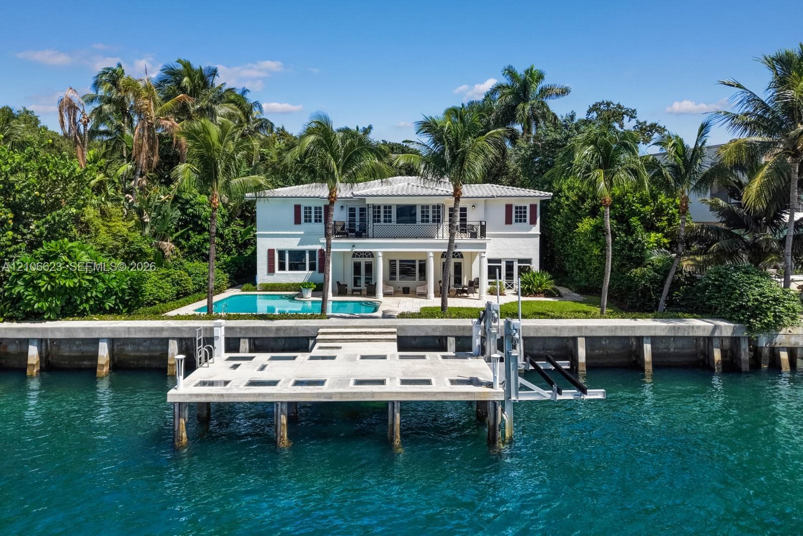 Waterfront residence featuring a private boat dock, pool, covered patio with structural columns, and balcony