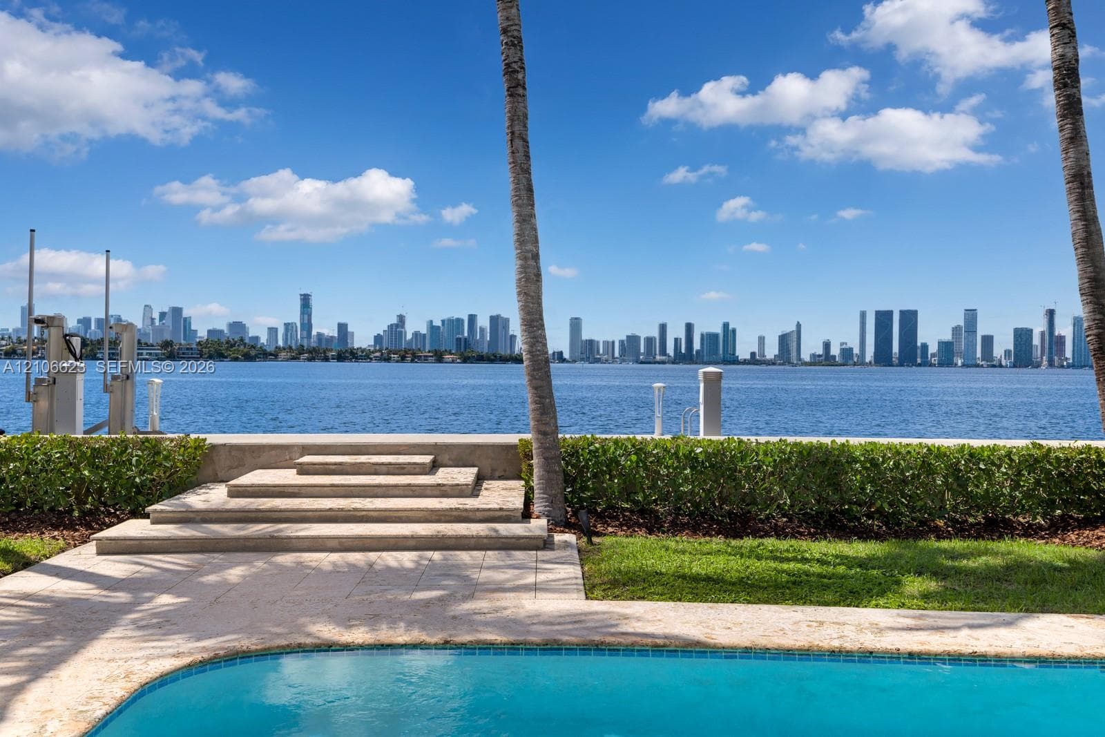 Waterfront property featuring a swimming pool, stone-paved decking, tiered stone steps, and manicured perimeter hedging