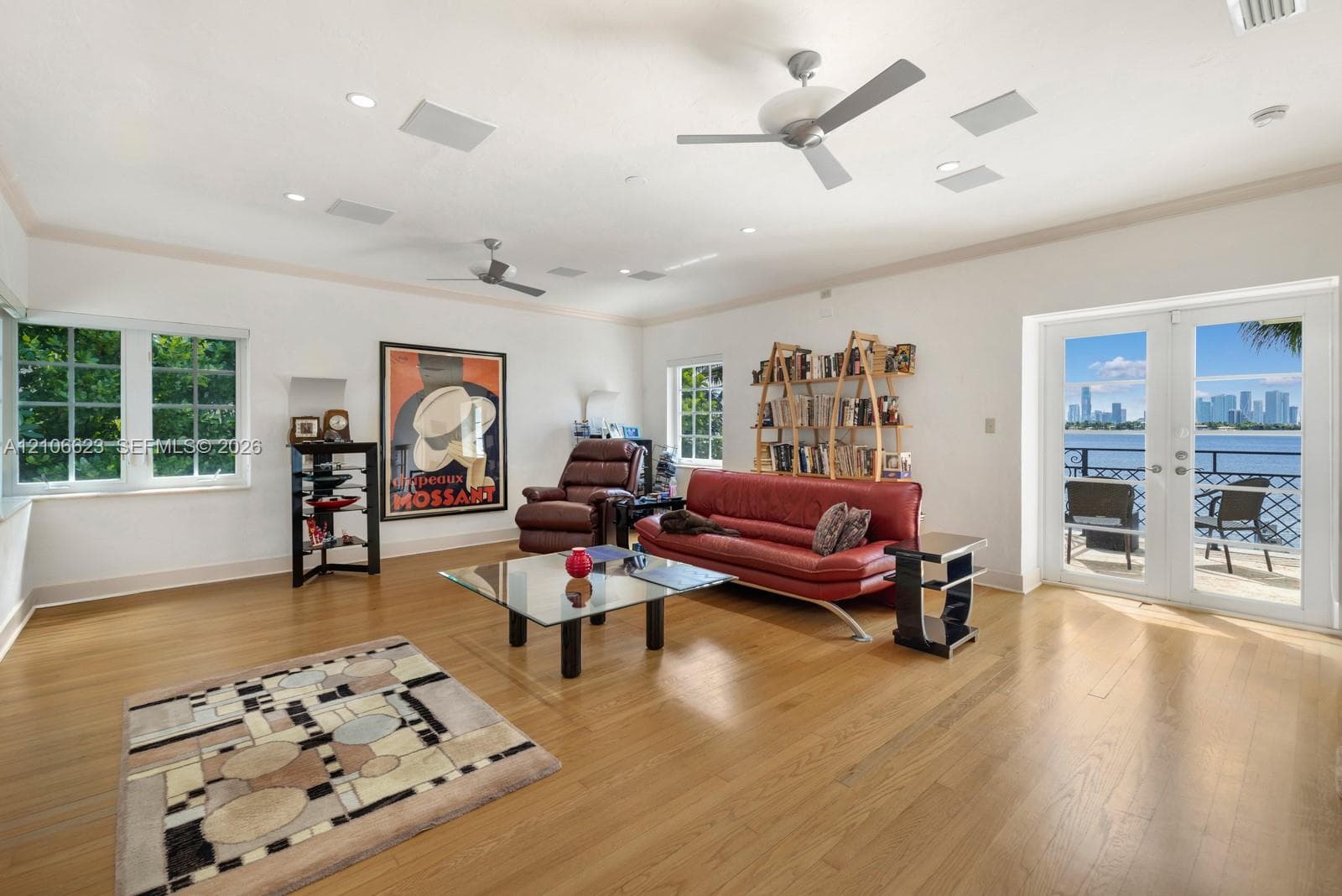 Spacious room featuring wood-finish flooring, multi-pane windows, dual ceiling fans, recessed lighting, and double-glass doors opening to a balcony with waterfront and skyline scenery