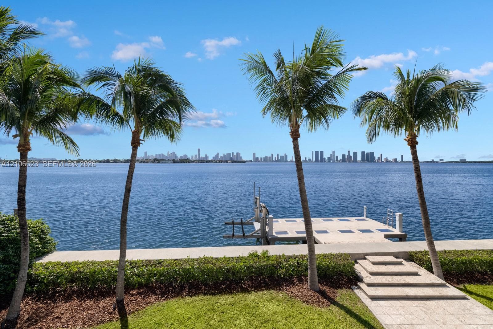 Waterfront property featuring a private dock, stone-paved walkway, manicured hedging, and mature palm trees